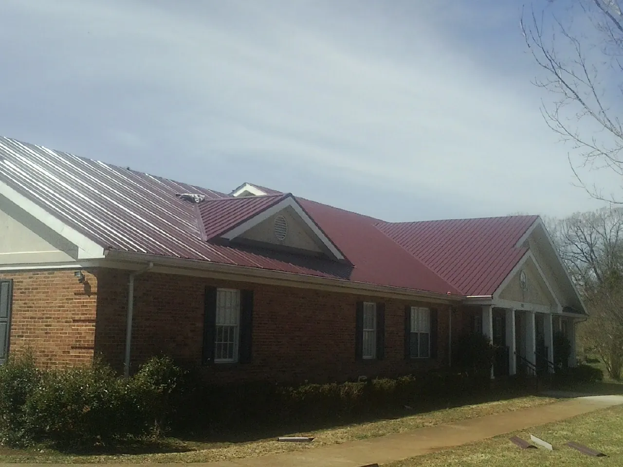 Red metal roof with gabled entries on a long brick building, from a Hail Damage Roof Repair job in Leighton