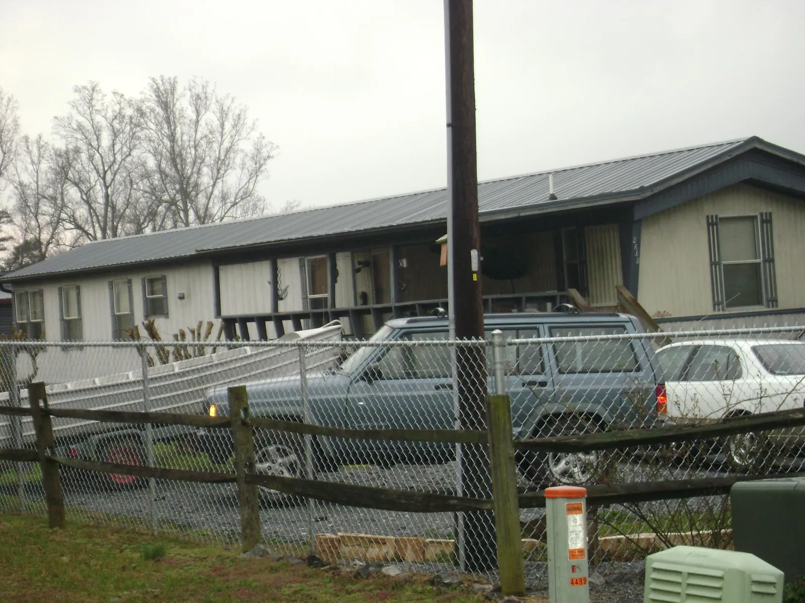 Dark metal roof on a long single story building behind a chain link fence in Leighton