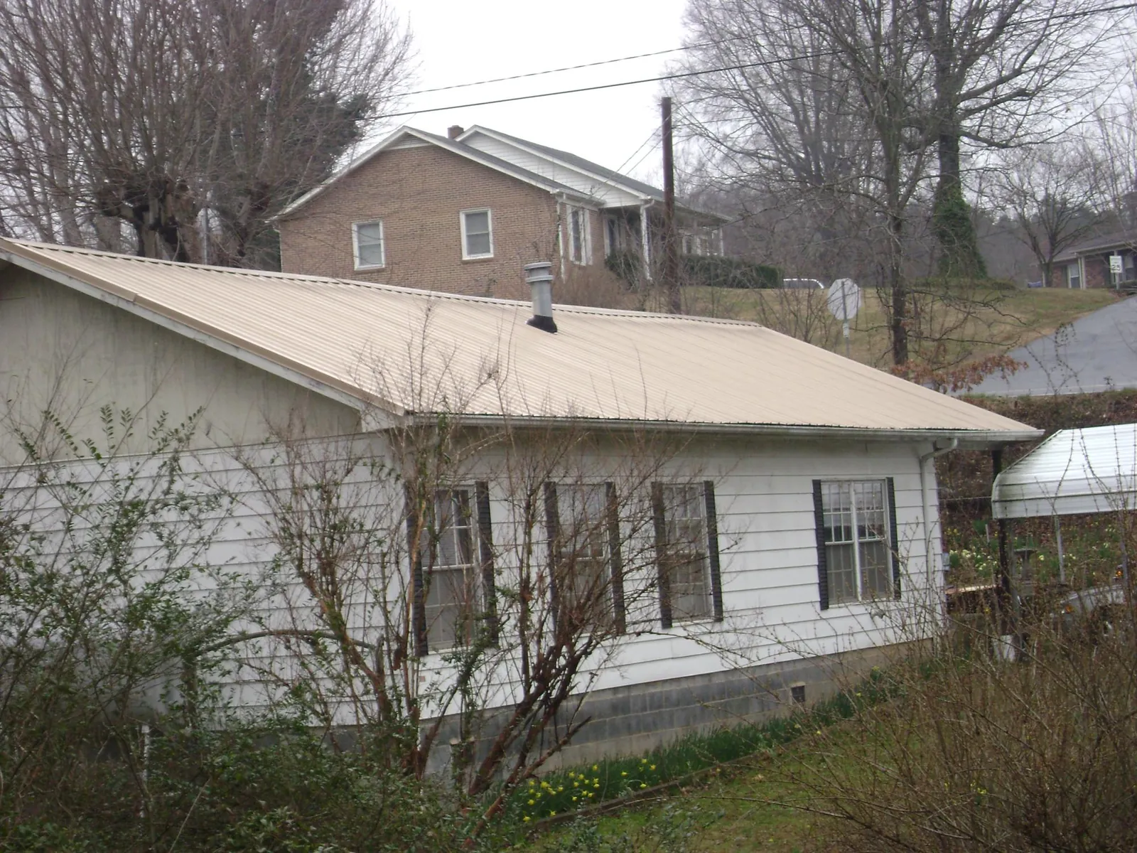 Tan metal roof on a white sided house set into a hillside — Commercial Roofing by Roofing Brothers in Leighton