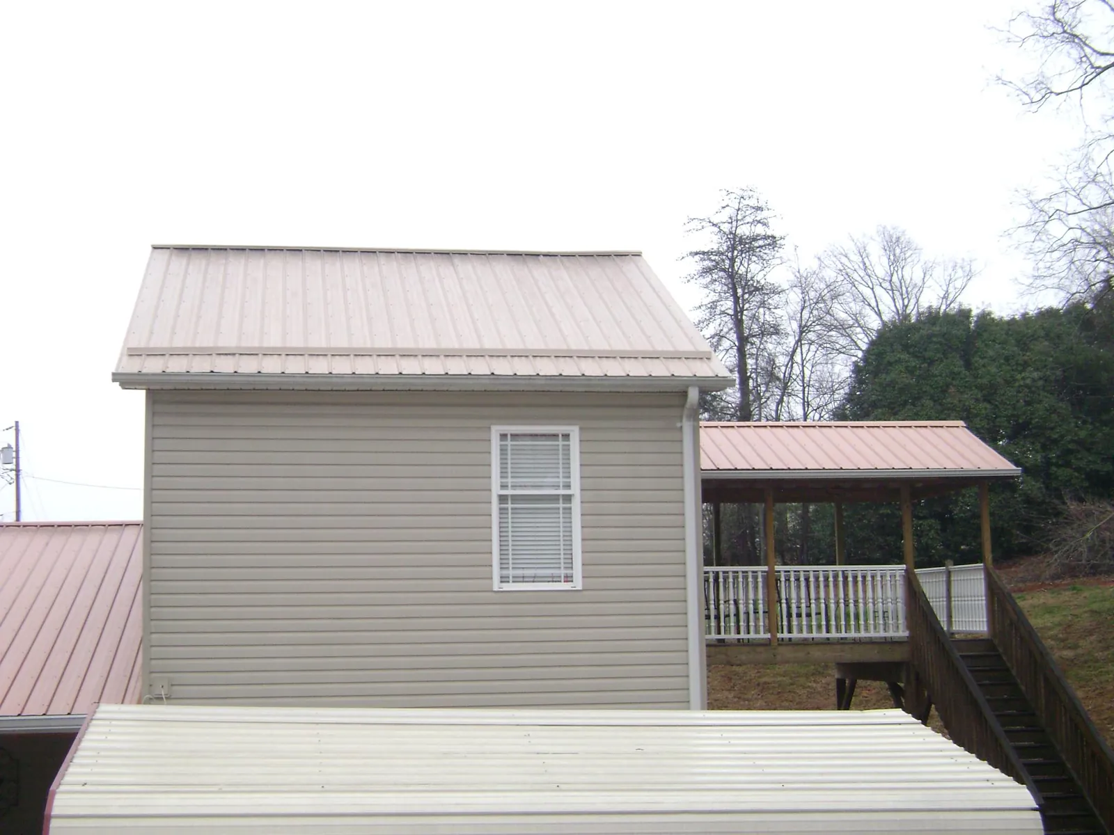 Tan metal roofs on a two story addition and attached porch, from a Roof Replacement job in Leighton